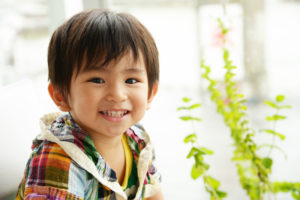 little boy smiling beside plant