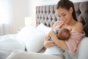 Happy mom sitting in bed, breastfeeding her baby