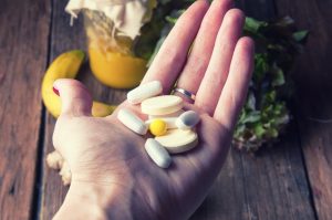 Supplements in person’s palm, nutritious food in background