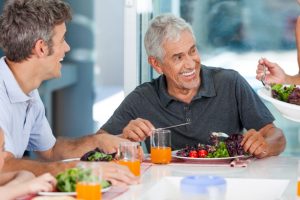 Older man with dental implants enjoying nutritious meal with friends
