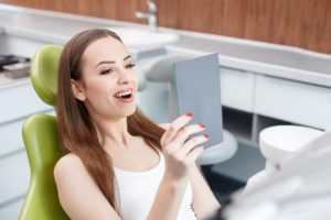 Patient visiting holistic dentist in Southlake, using mirror to admire her teeth