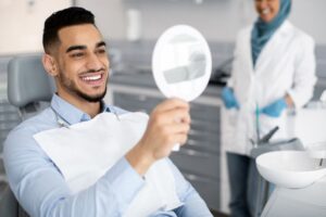 Happy dental patient looking at his smile in mirror 